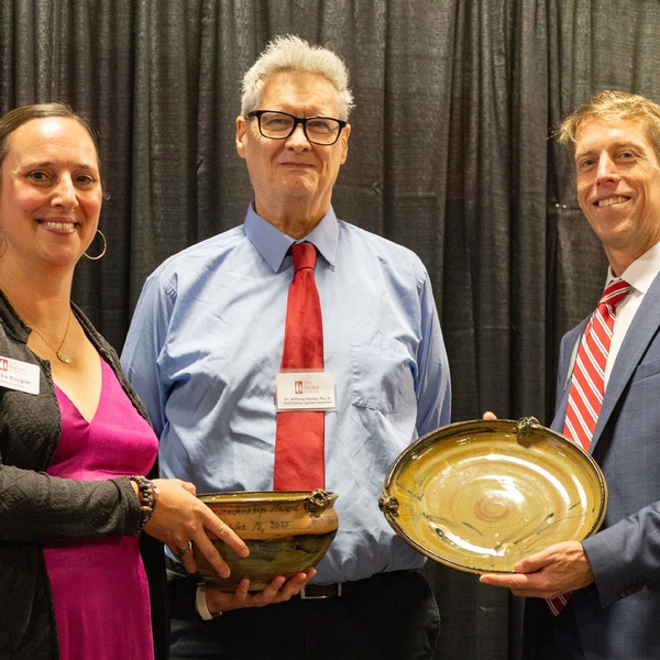 A man in a red tie and blue shirt stands proudly while leadership from The Siena School present him with awards during an annual school celebration. Everyone is happy.