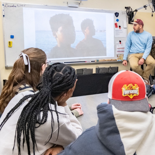 A guest speaker in a photography class at The Siena School sits at the front of the room discussing his work. Students look on interestedly.