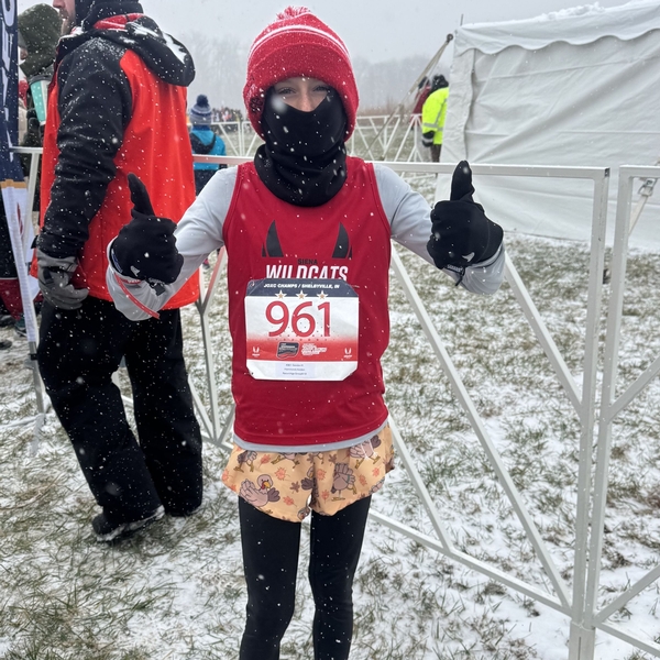 A 5th grade boy from The Siena School stands on a snowy field giving a thumbs up. He is about to run a national cross-country race.