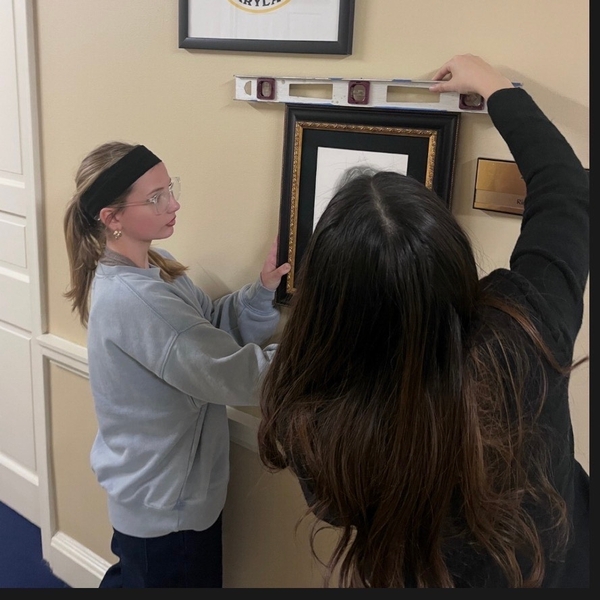 An 8th grader from The Siena School helps hang a framed drawing she did in the Maryland General Assembly building.