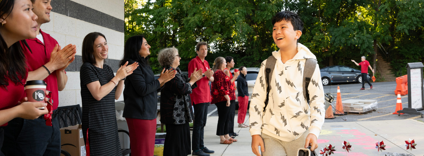 A student walks into school on the first day while a line of adults smile and clap.