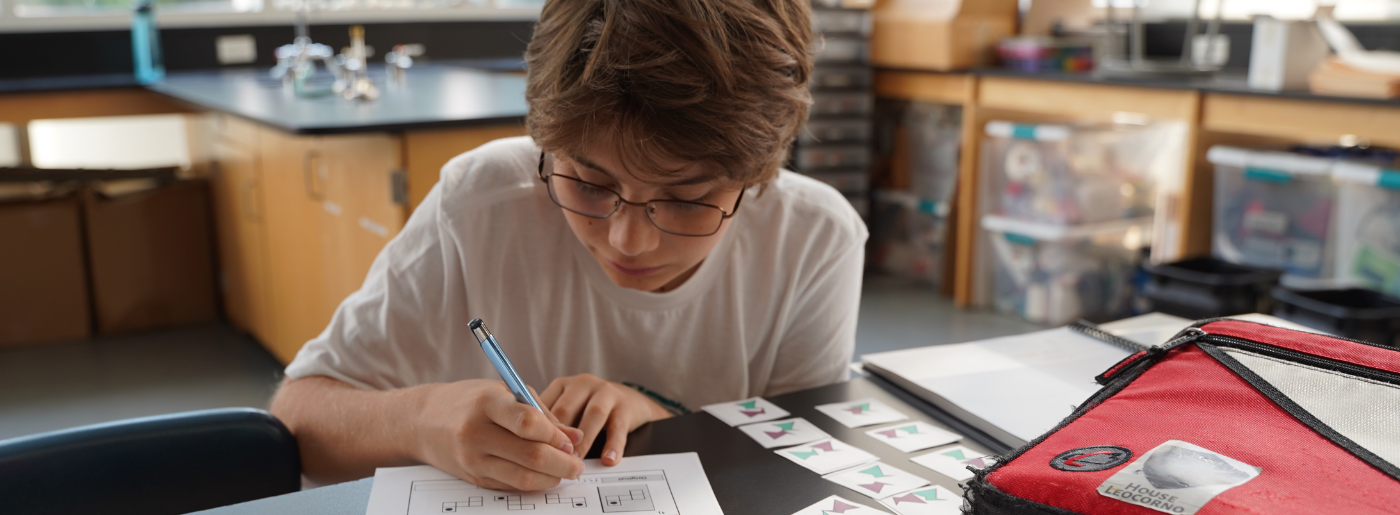 A student writes on a piece of paper in a science classroom. He is focused and intent.