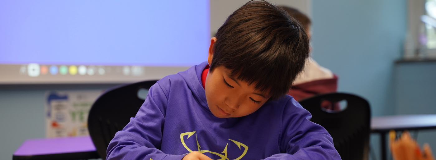 A boy sits at a desk and writes.