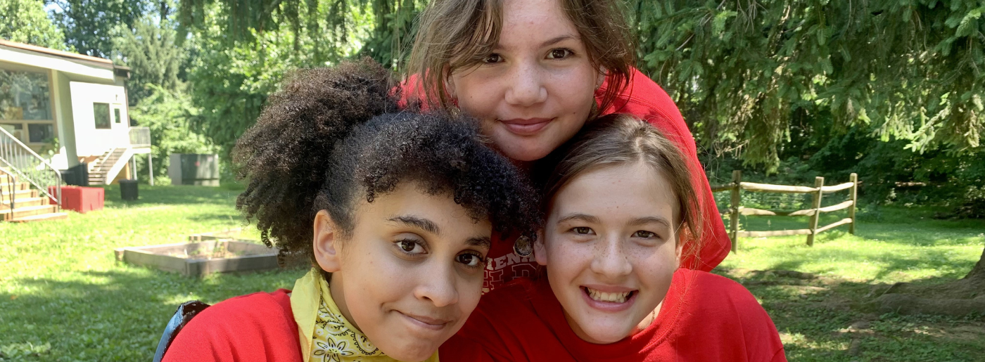 Two girls look ahead and smile while a third girl rests her head atop the other two. They are all ha