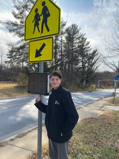 A high school student stands proudly in front of a speed monitor that he advocated to install to improve safety.