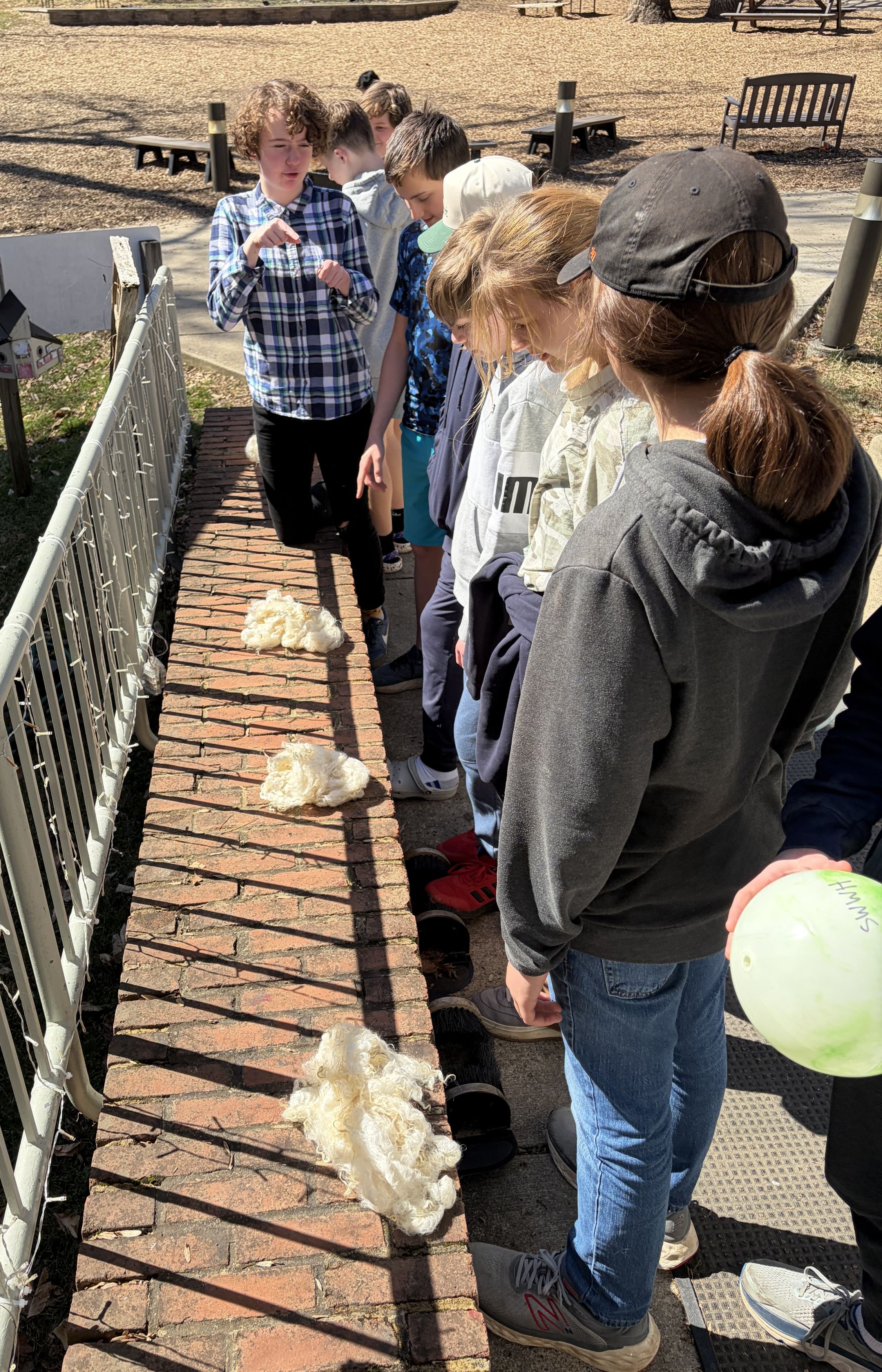 Students stand outside in the sun checking on their drying wool.