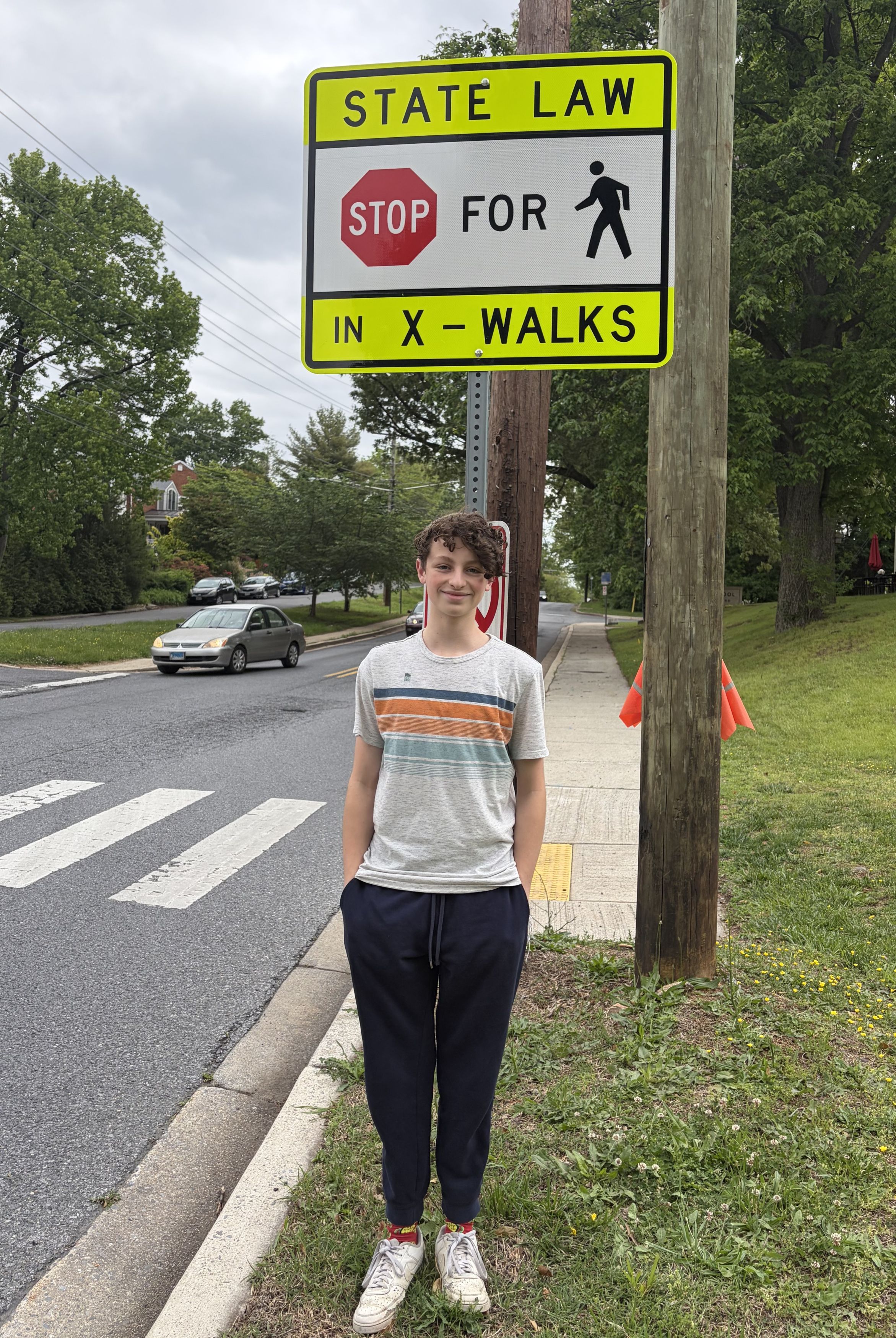 A student looks proudly at the camera as he stands next to a pedestrian crossing sign.