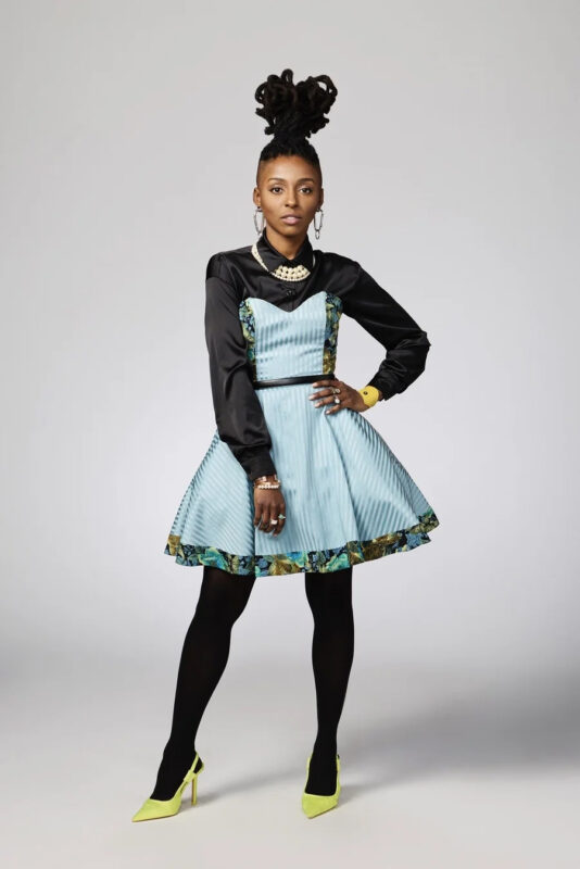 A Black woman in a colorful blue dress stares confidently at the camera.