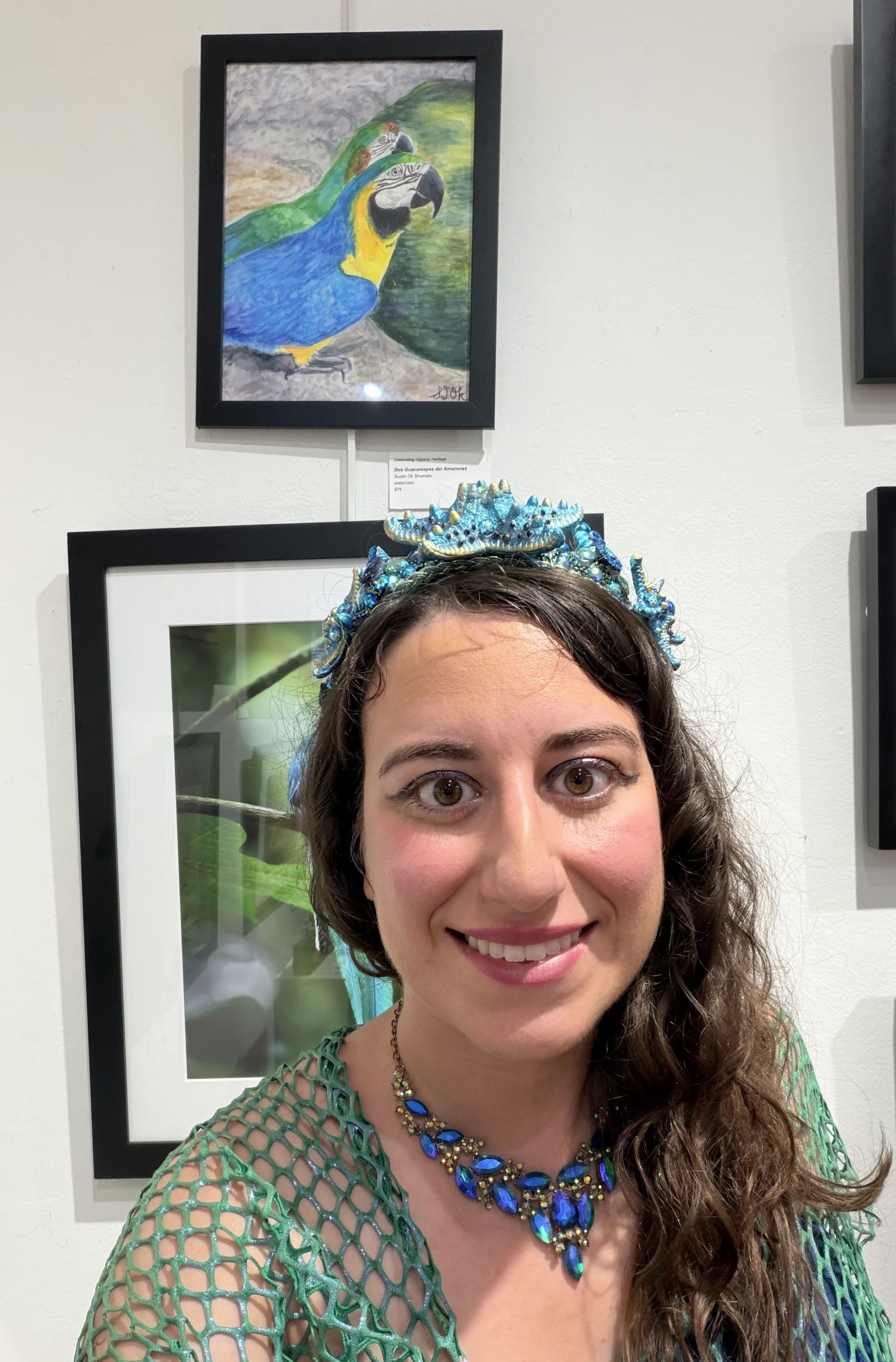 A woman smiles at the camera while standing in front of framed art in a local gallery.