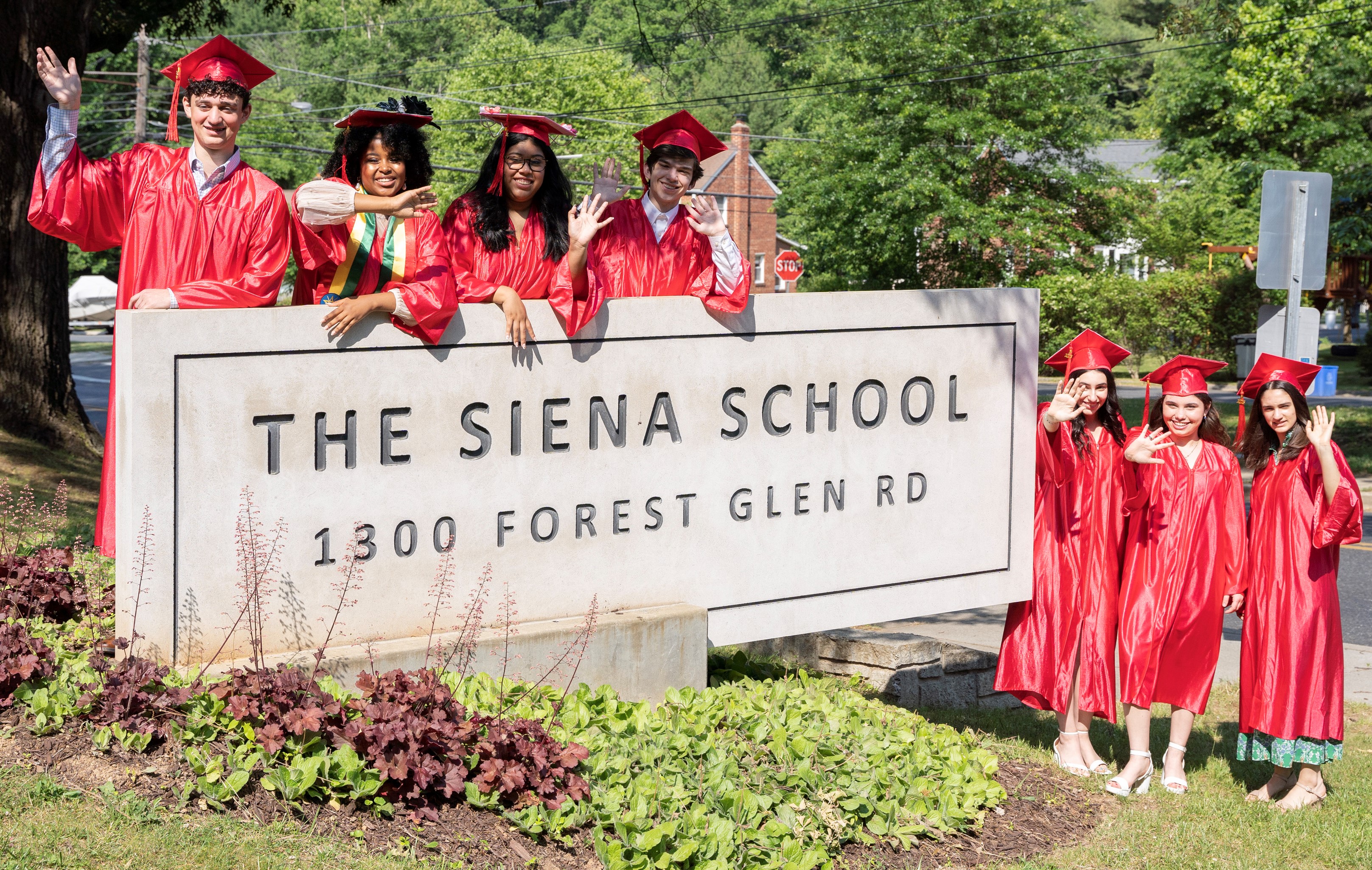 Siena high school graduates in red caps and gowns wave on Graduation Day 2023.
