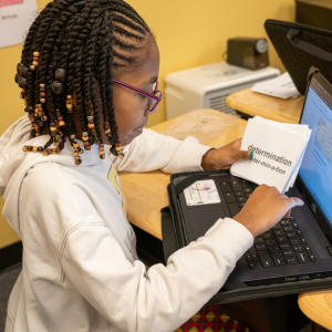 A girl in glasses works on a laptop at a desk. She is very focused.