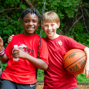 Two boys in red shirts smile at the camera while on the school playground.