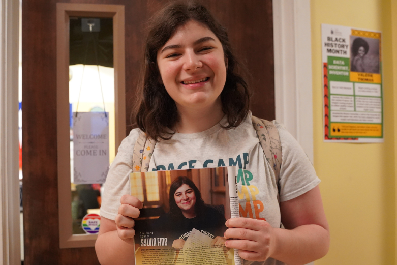 A high school student beams at the camera and holds a magazine featuring herself being honored.