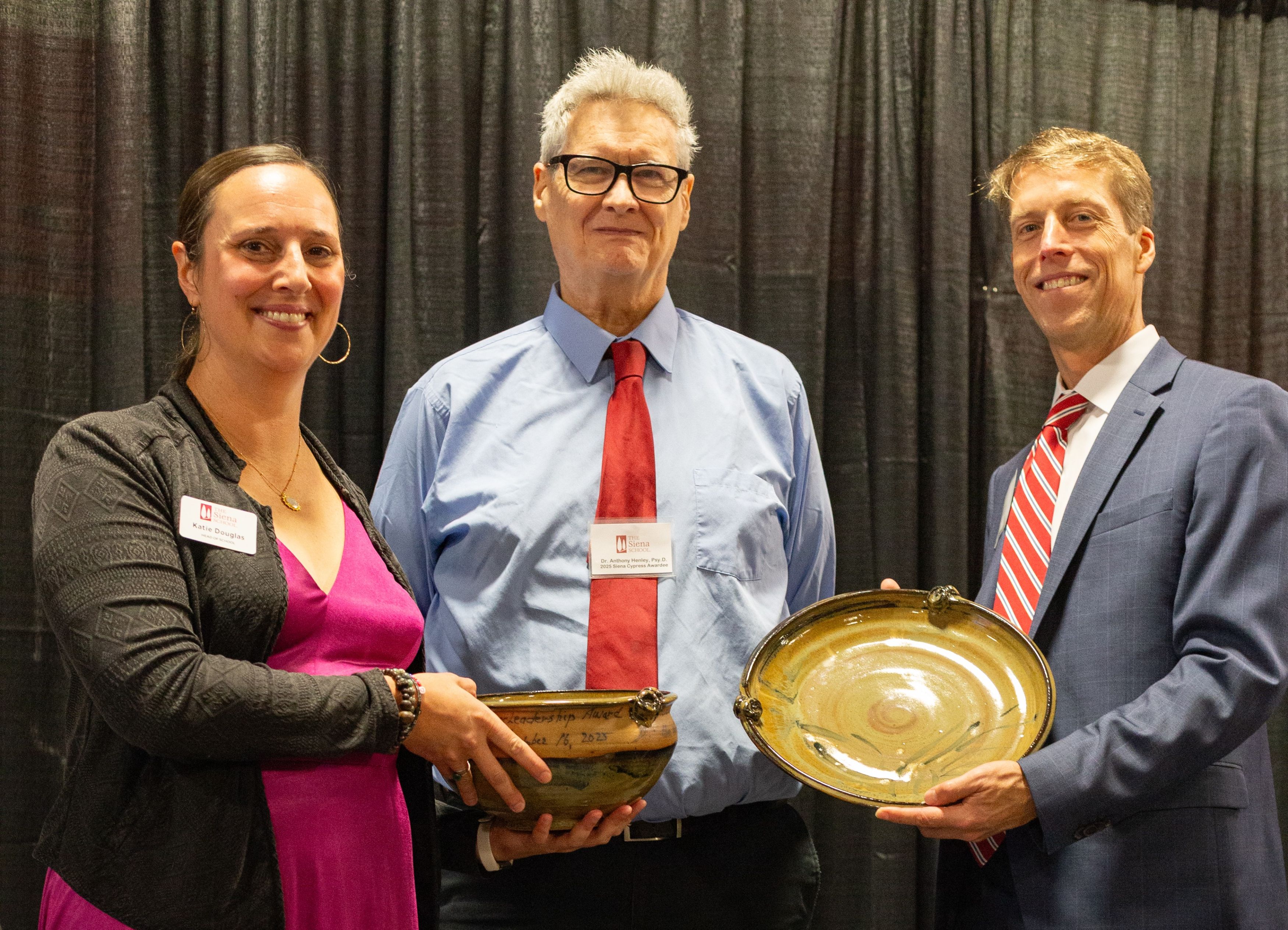 Three people stand together smiling in front of a black curtain during a school awards ceremony.
